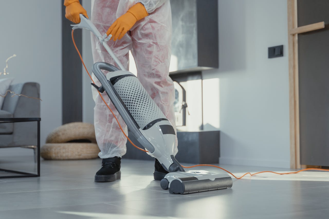 our-story A person in protective attire cleaning a modern room with a vacuum. Bright and tidy atmosphere.