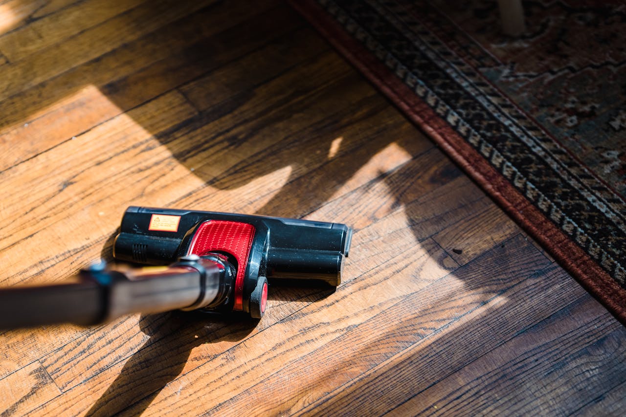 gallery-01 Close-up of a vacuum cleaner on wooden flooring near a patterned rug, showcasing domestic cleaning.